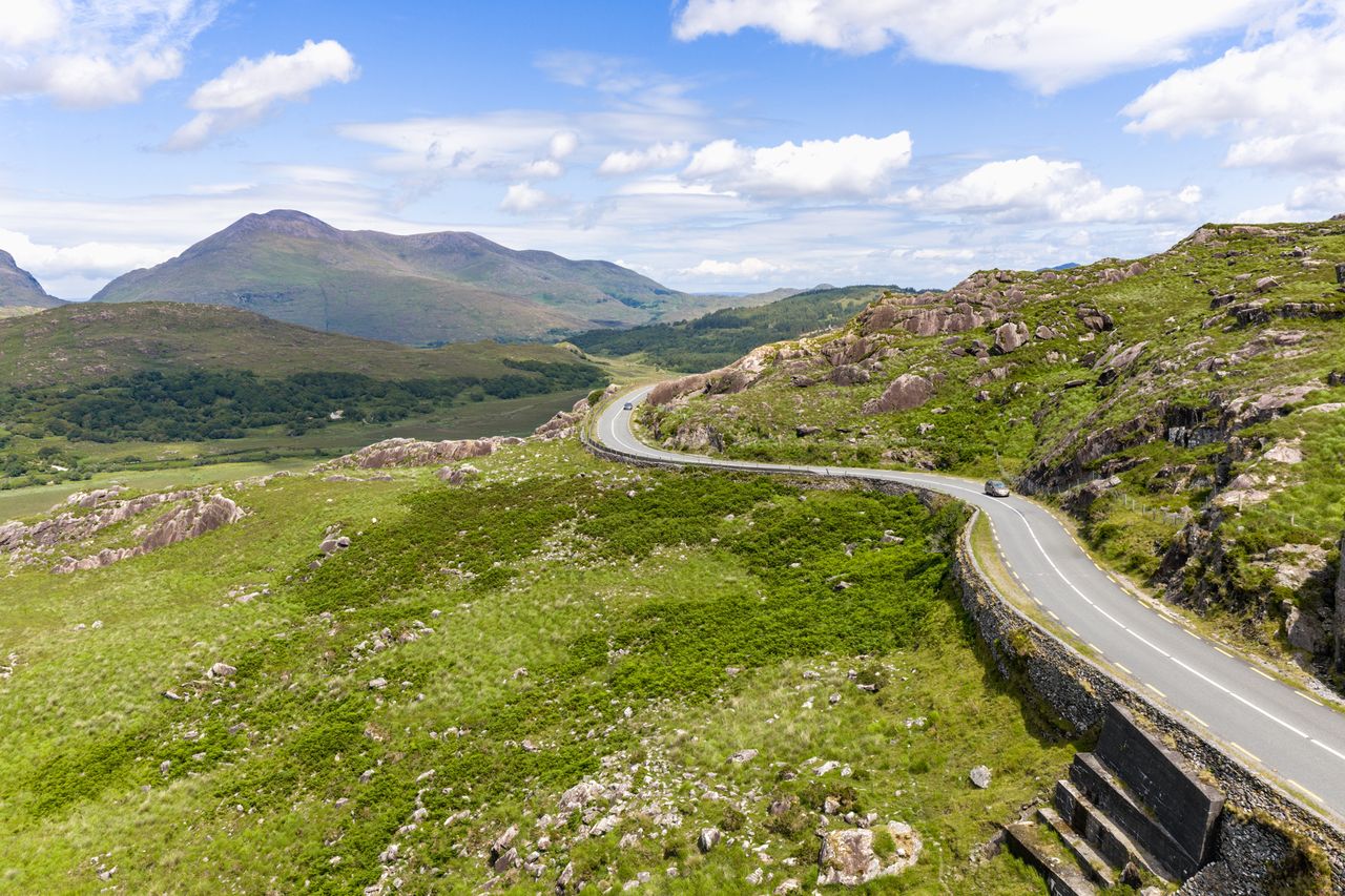 Scenic winding road through a green hilly landscape under a blue sky part of the Ring of Kerry in Ireland