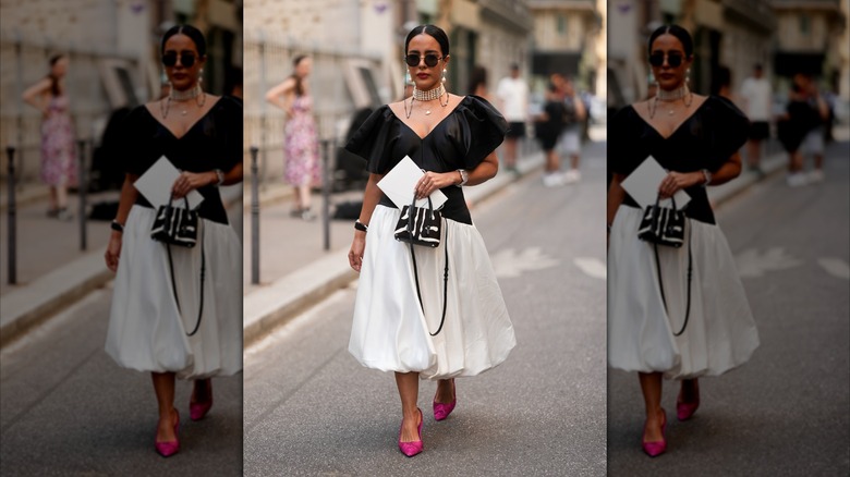 A woman wearing a black and white dress, a multi-string pearl choker, black sunglasses, and bright-pink heels.