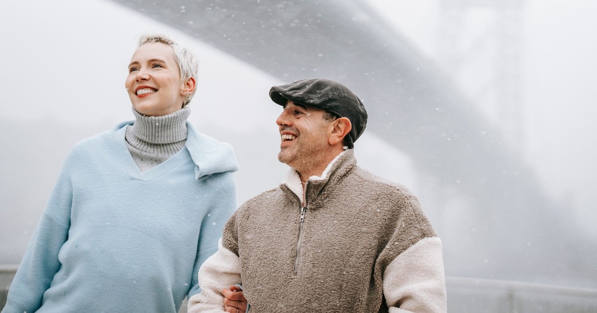 Cheerful adult man with girlfriend talking and looking away against city bridge on misty day