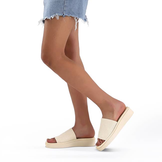 Person wearing frayed denim shorts and the slide sandals in beige