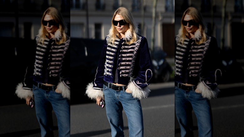 A woman wearing a military-style coat with fur sleeves and a fur collar with jeans and a black belt.