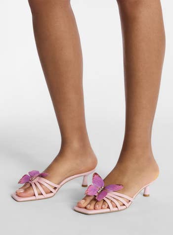 Someone wearing strappy heeled sandals with butterfly accents on the toes