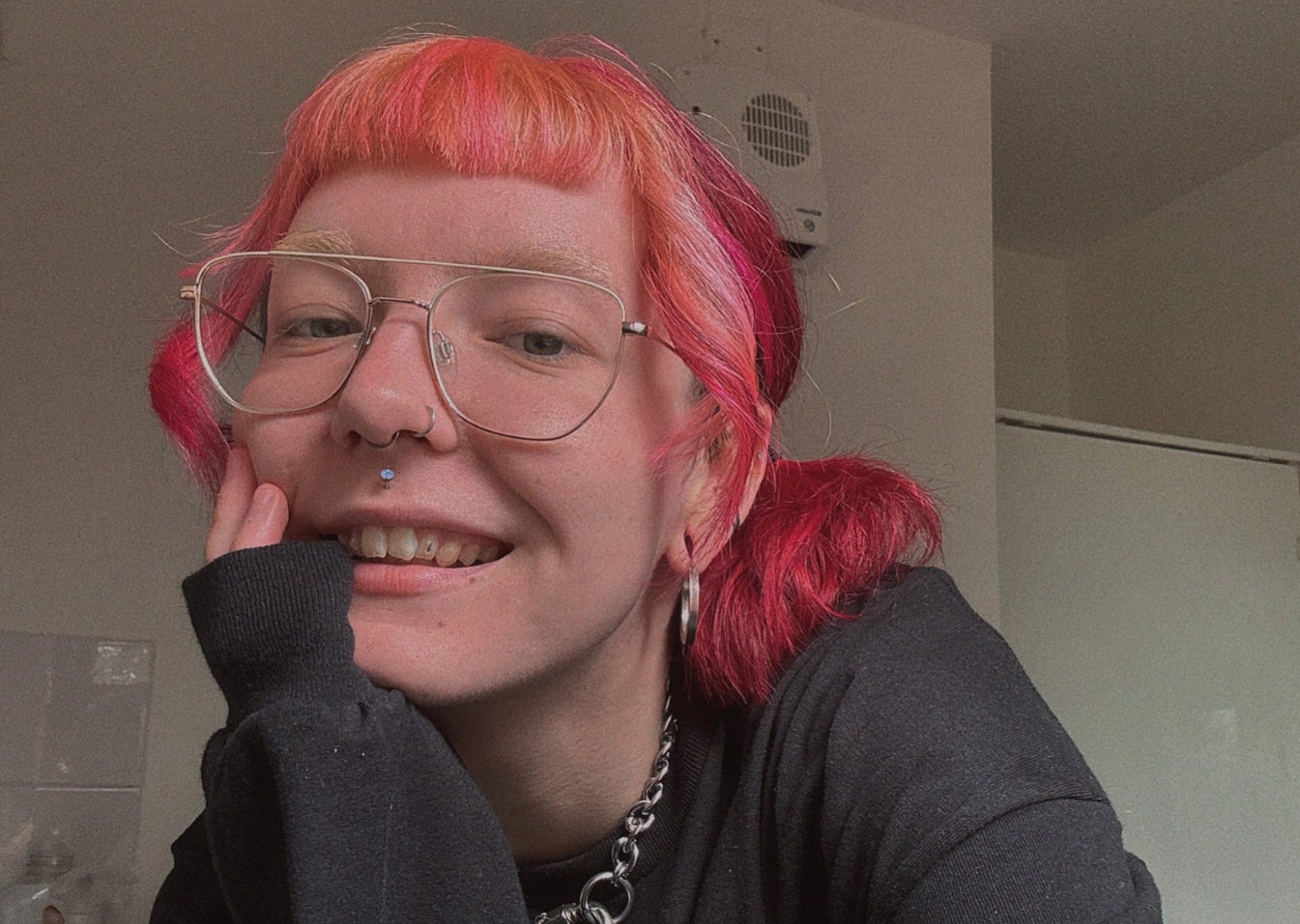 Dee Whitnell taking a selfie at home with pink hair, resting their chin on their hand