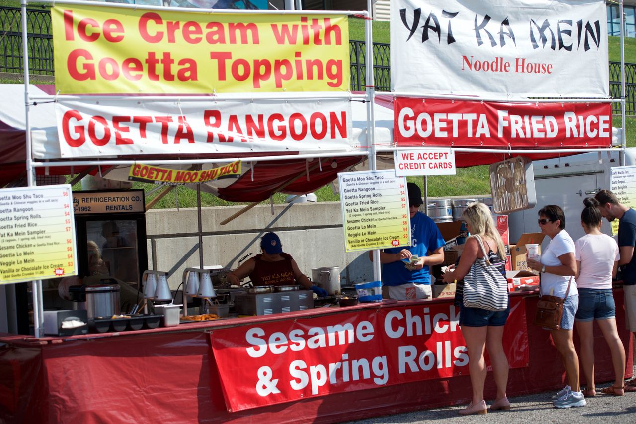 Food vendor booths at an outdoor event offering dishes with Goetta with people standing to order