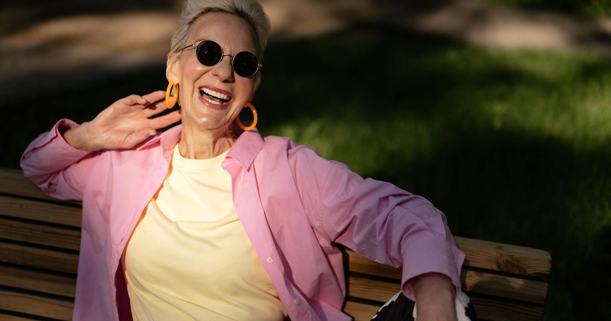 Chic elderly woman laughing and relaxing on a park bench under the sun.