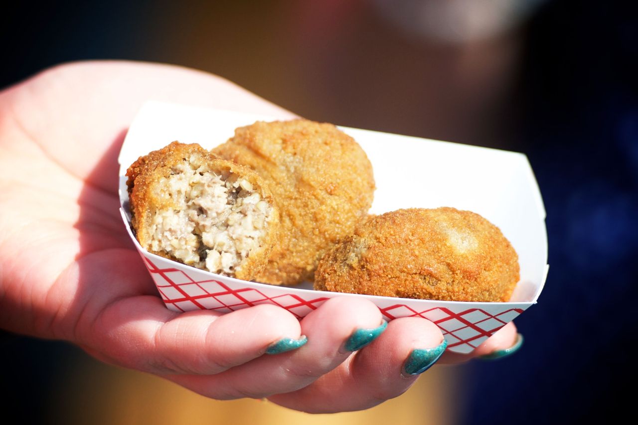 A hand holding a food tray containing breaded stuffed balls possibly Goetta