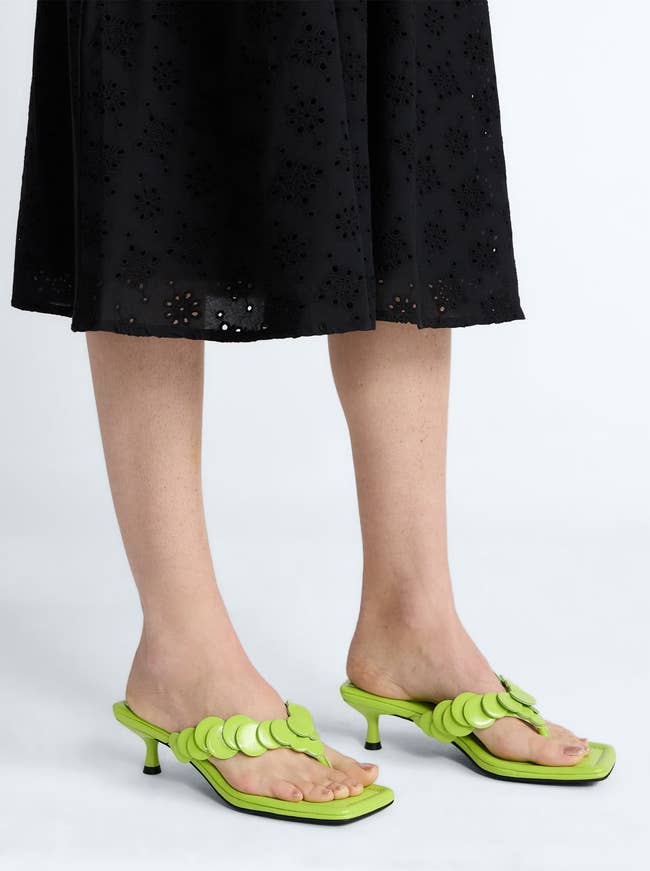 Person wearing green heeled sandals with scalloped design and a black eyelet skirt