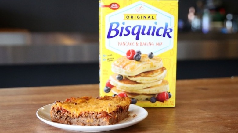 A slice of burrito Bisquick bake casserole on a plate next to a box of Bisquick pancake and baking mix
