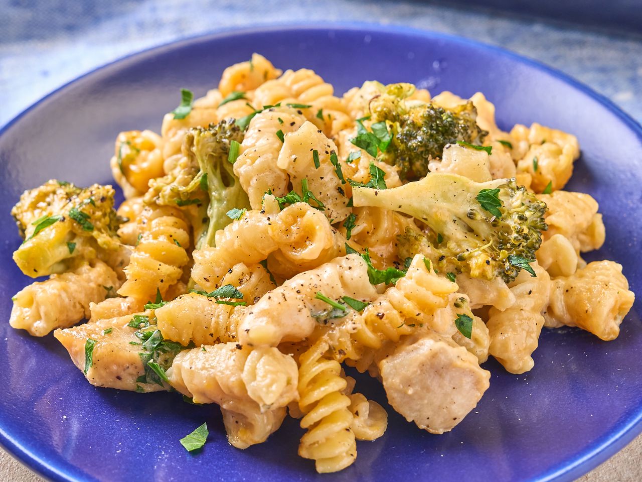 Pasta with chicken broccoli and a cheese sauce served on a blue plate