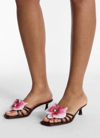 Person modeling open-toed sandals featuring a large decorative flower on the straps