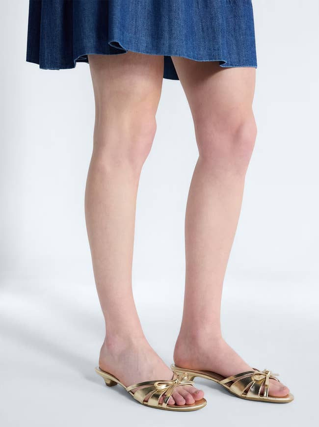 Person wearing a knee-length denim skirt and gold strappy slide sandals
