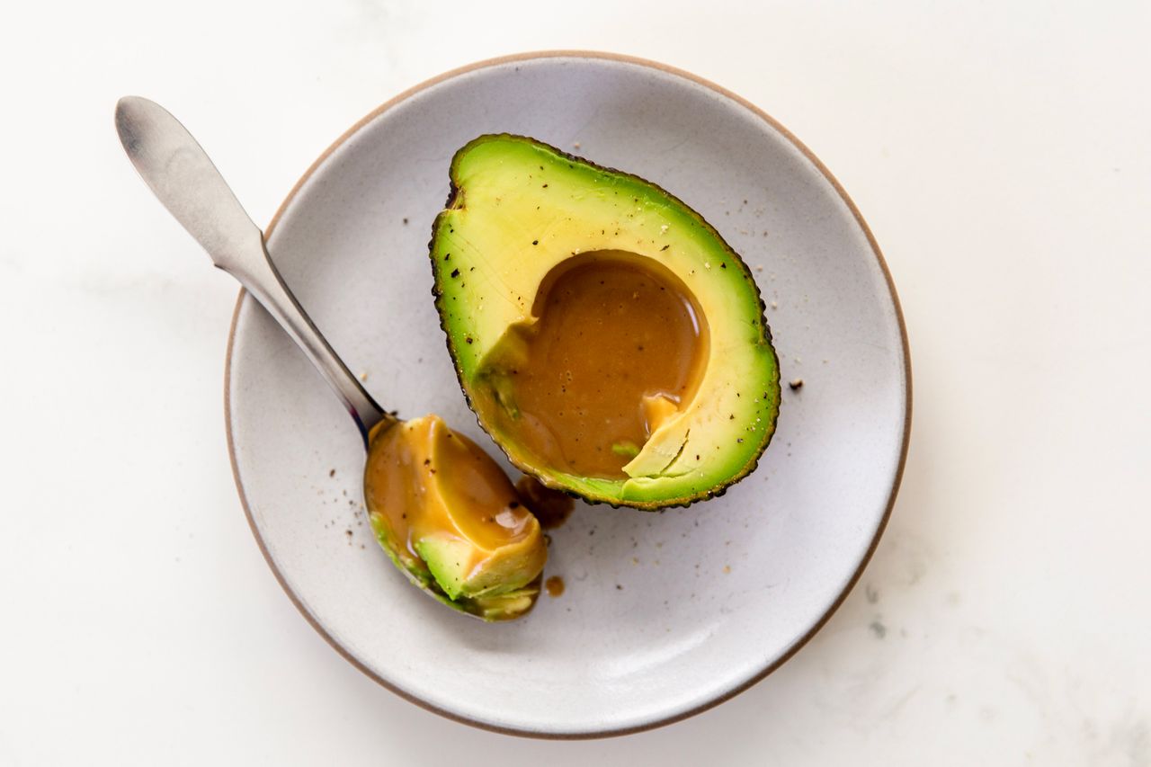 Avocado half with sauce on a plate spoon beside it