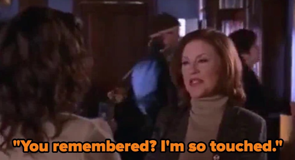 A woman with styled hair, wearing a turtleneck and blazer, speaks to another person. Text reads: