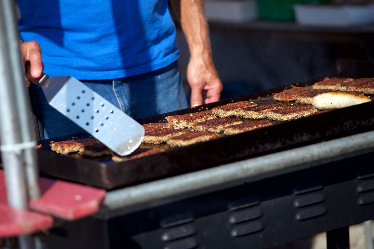 Closeup of a person grilling Goetta patties on a flattop grill