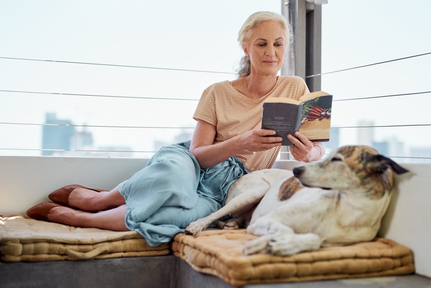Next to dogs, books are my best friends. Shot of a mature woman reading a book on her balcony with her dog next to her at home.