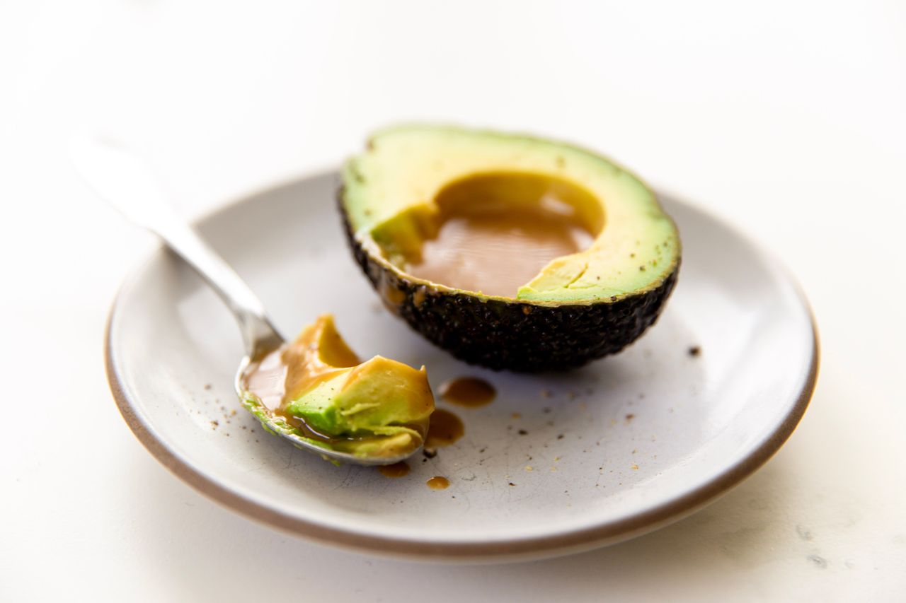 Avocado with a scooped out section filled with sauce served on a plate with a spoon beside it