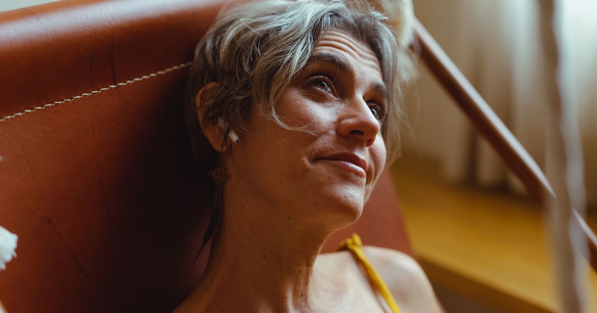 Elderly woman enjoying leisure time indoors, listening to music with wireless earbuds.