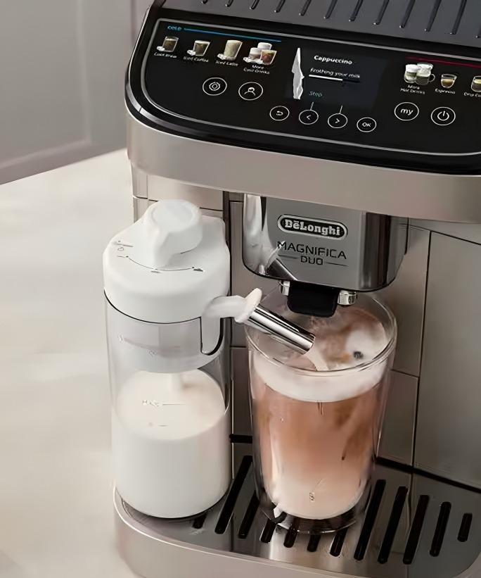 A De'Longhi coffee machine in black and stainless steel with a glass of iced coffee on the drip tray beside an automatic milk dispenser.