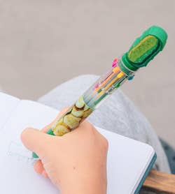 Child using a multicolor pen with a fun pineapple design to write in a notebook. Text reads: