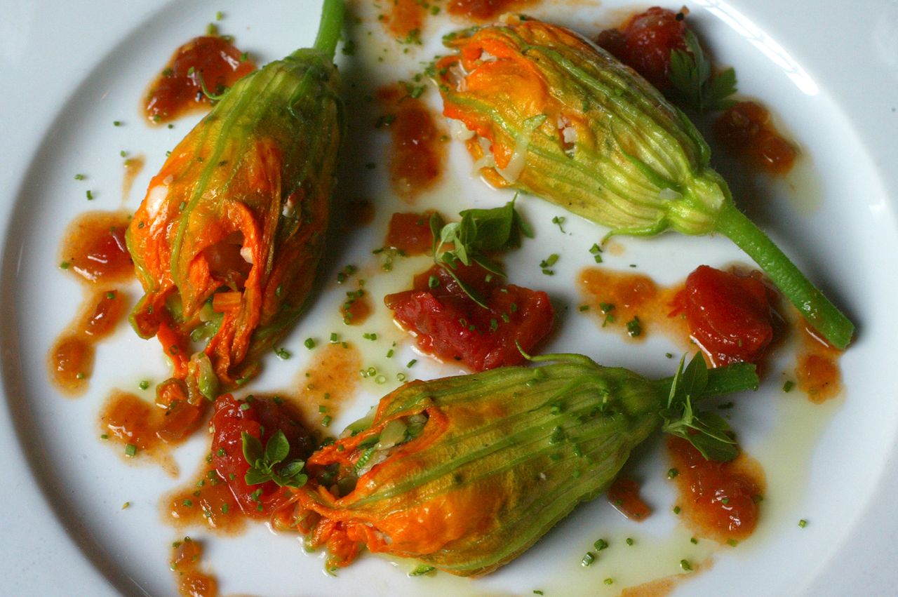 Stuffed zucchini flowers on a plate with tomato sauce and garnishes