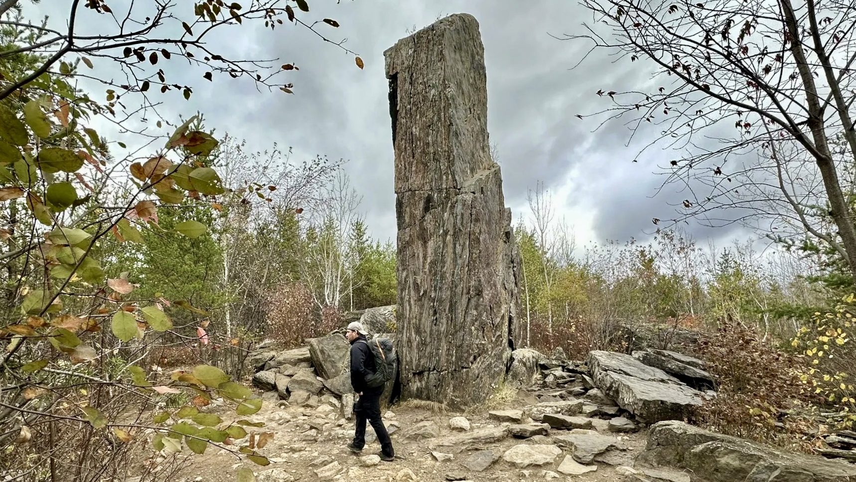 A man in dark clothes walks along a rocky trail in front of a magnetic monolith in northern Minnesota.
