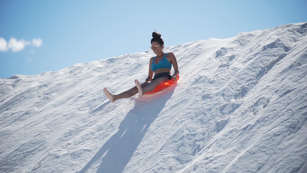 a woman on a sled sand boards down a white gypsum dune at White Sands National Park, New Mexico