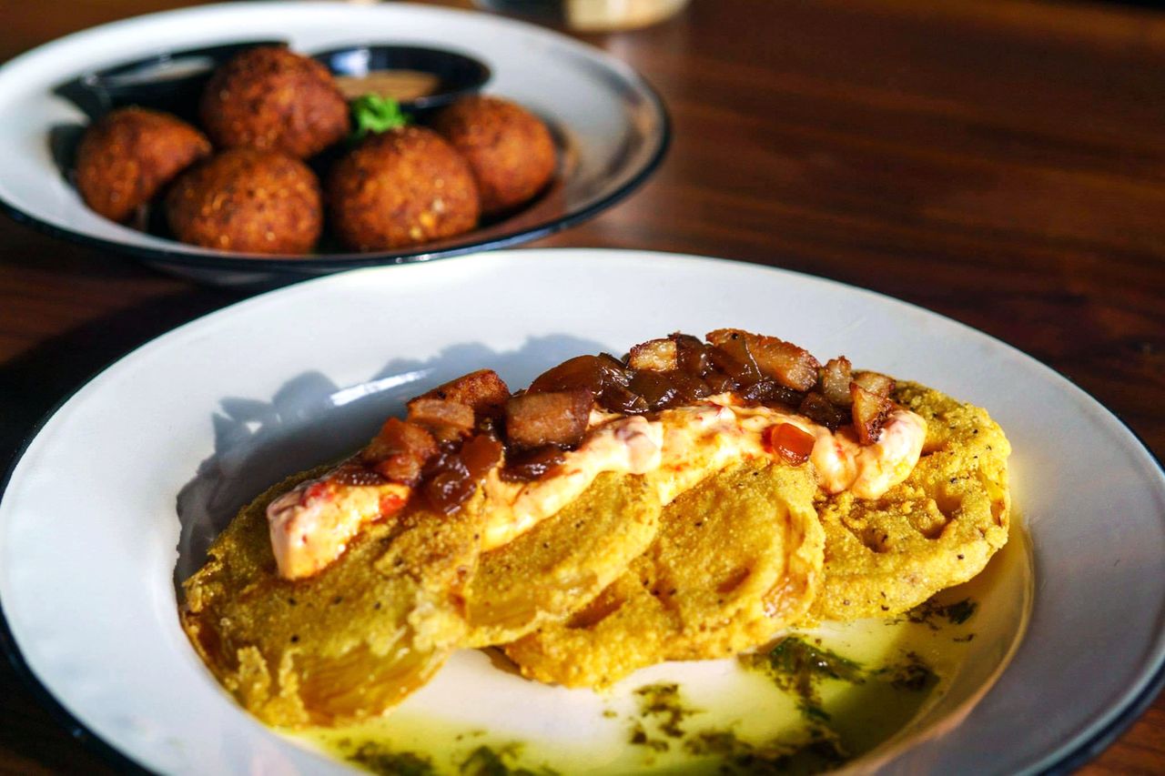 Plated meal featuring fried green tomatoes with toppings and a side dish with fried goetta hushpuppies