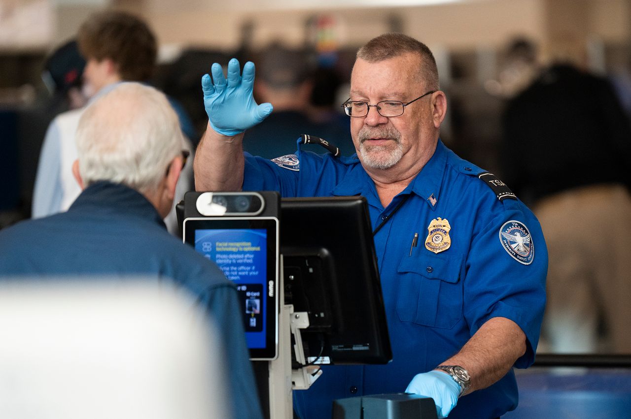 TSA officer assisting a traveler at a security checkpoint using identification verification equipment