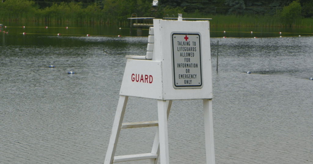 A white lifeguard stand and safety sign overlooking Plamann Park swimming lake in Wisconsin.