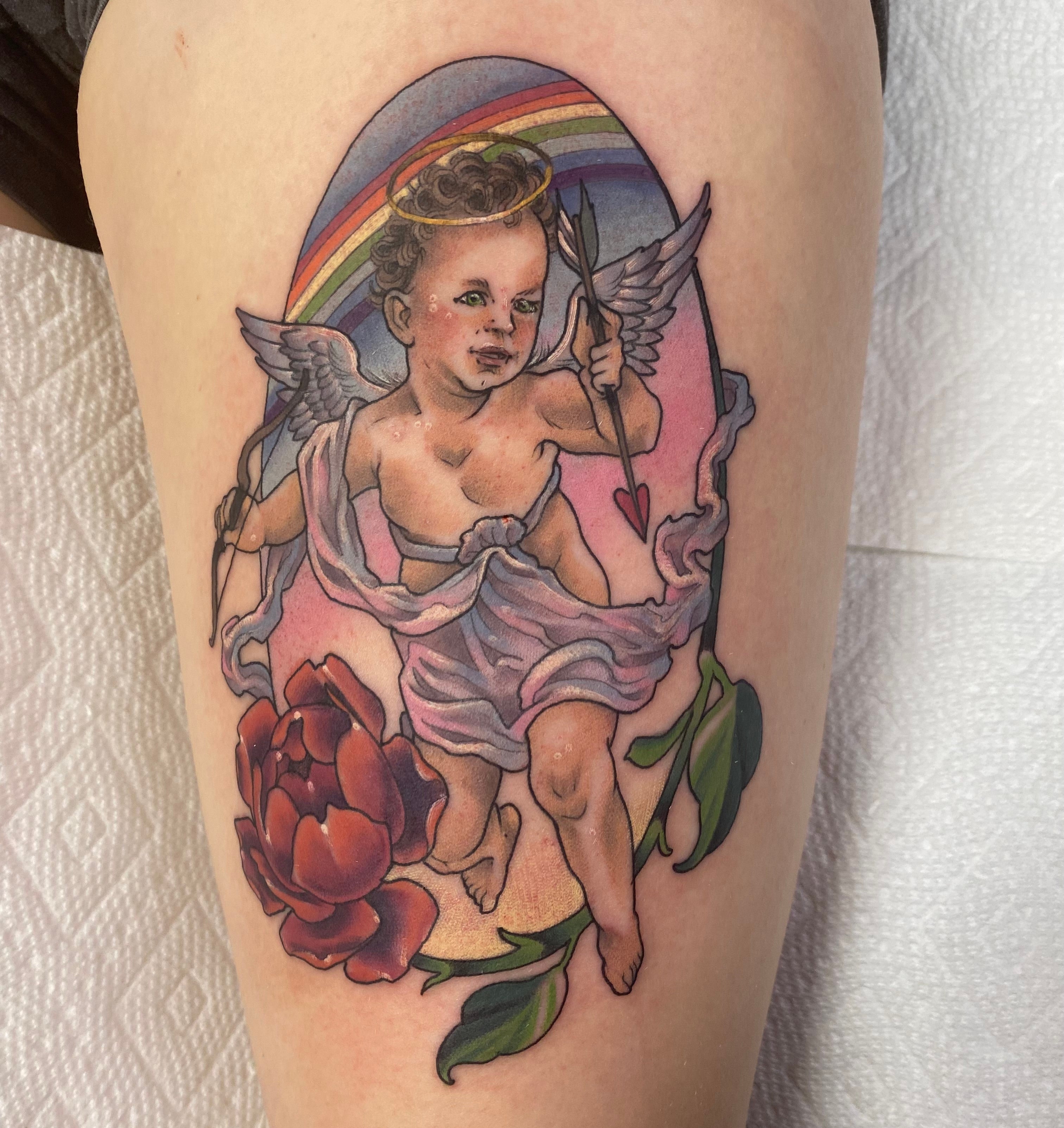 My tattoo for Eddie of a cherub holding a heart-ended arrow with floral and rainbow details on my thigh