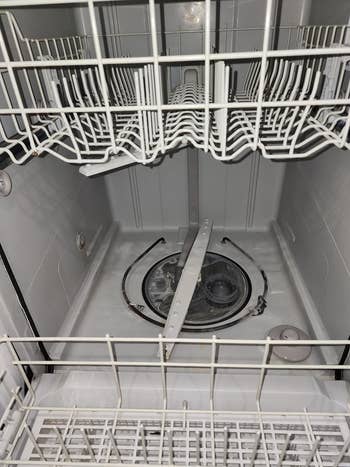 Open dishwasher with empty racks, focusing on the spray arms and interior, showcasing cleaning or maintenance angle