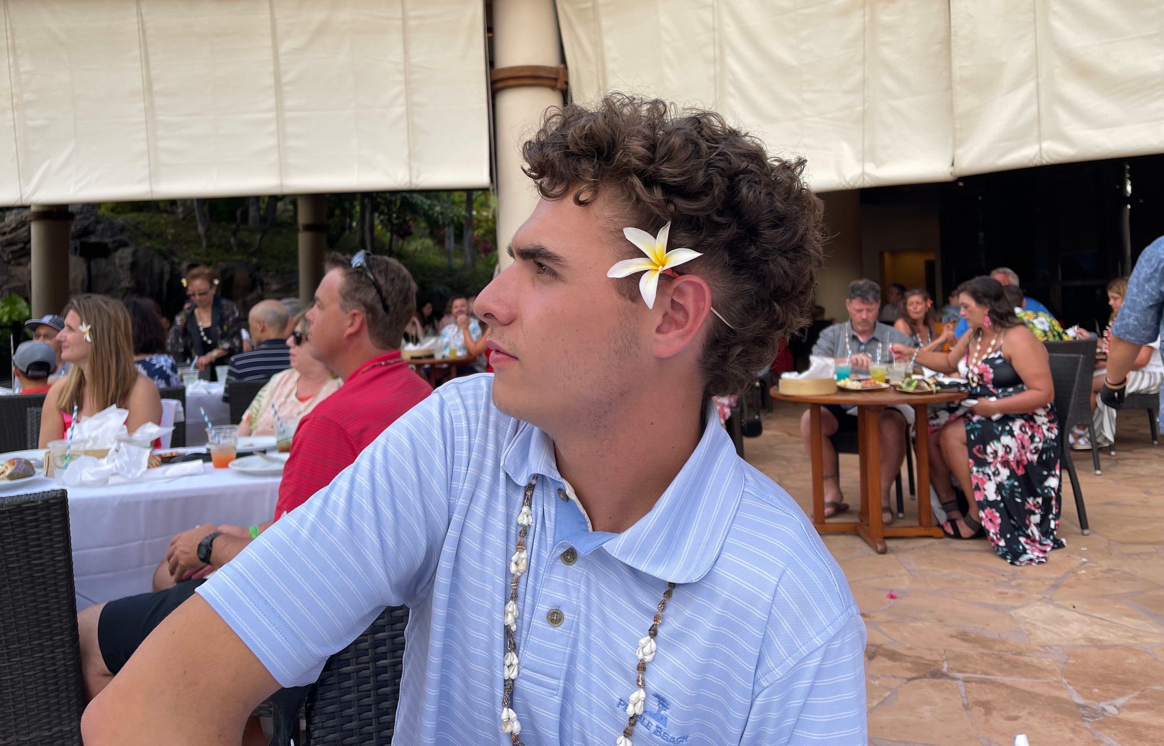 Eddie with a flower in his ear looks off to the side at an outdoor, beachy gathering