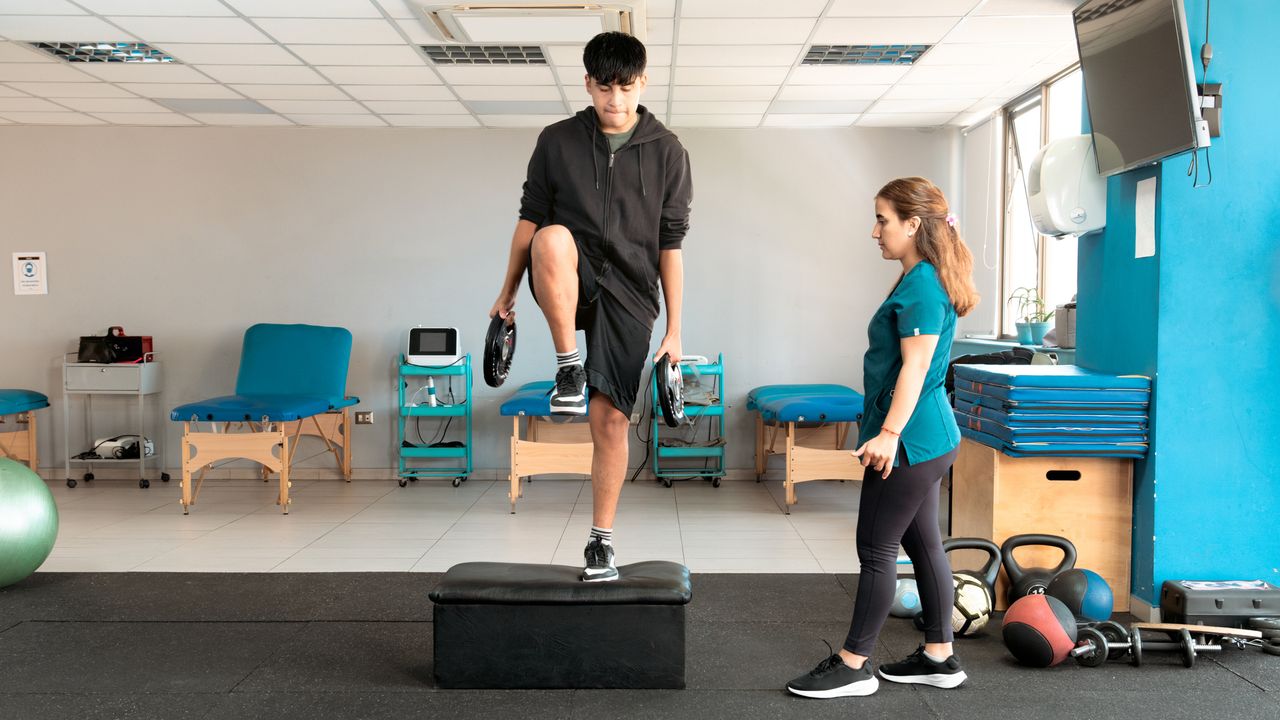 Medical professional observes a man performing the step-up exercise, holding weight plates by his sides