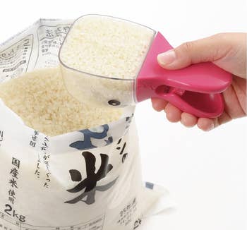 Hand scooping rice with pink measuring cup from open rice bag; Japanese text reads
