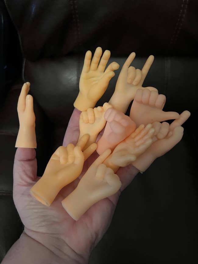 A hand holding small, realistic toy hands posed in different gestures, showcasing unique novelty items for possible purchase