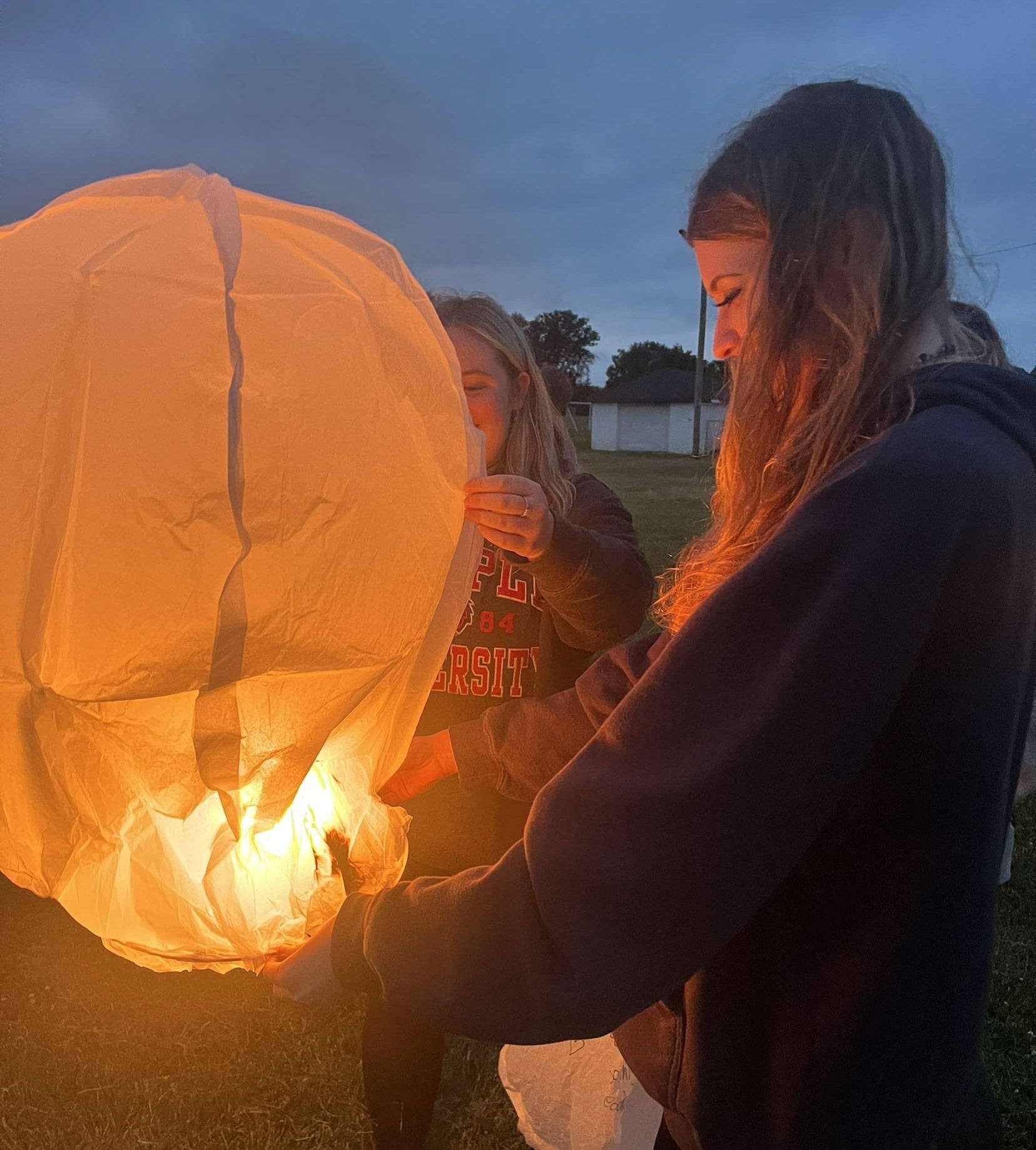 My friend and me holding a glowing paper lantern outside at dusk