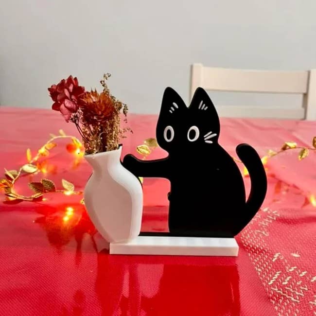 Decorative black cat-shaped vase holder with dried flowers on a table decorated with string lights