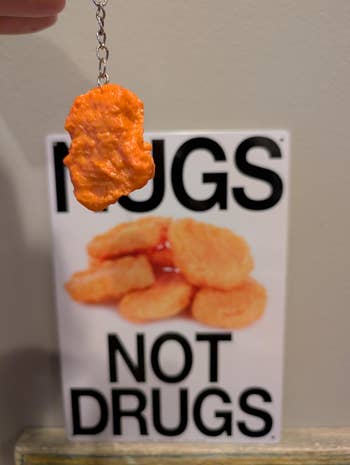 Keychain of a chicken nugget, with a sign in the background reading
