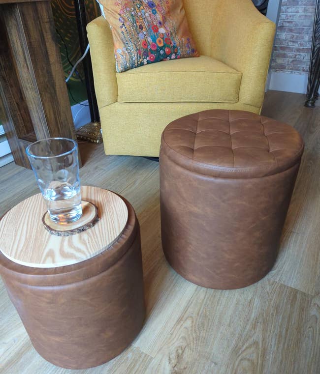 Two round leather stools; one holds a glass on a wooden top
