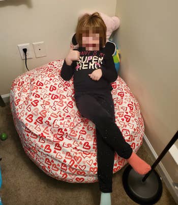 same corner with the stuffed animals in a bean bag with heart designs and a child sitting on top