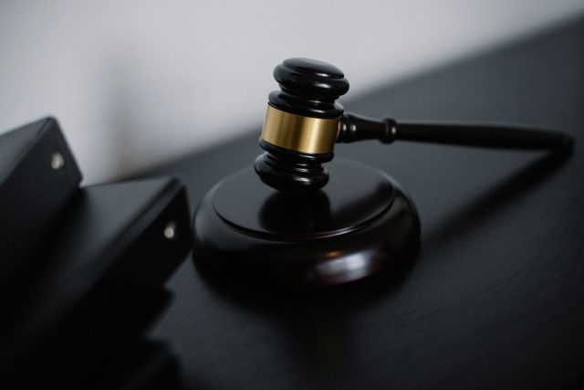 High angle of shiny wooden ceremonial mallet with golden detail placed on judge tale near documents folders
