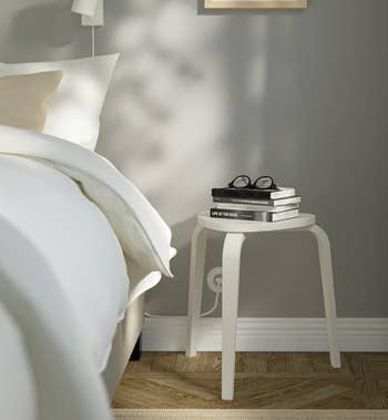 Minimalist bedroom with a white stool being used as a side table with books and glasses stacked on top