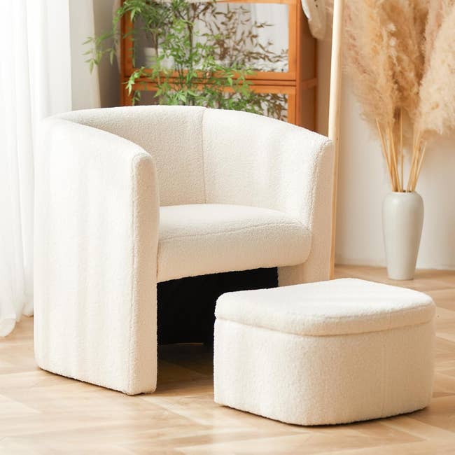 A cozy armchair with matching ottoman, upholstered in soft fabric, set on a wooden floor next to decorative plants