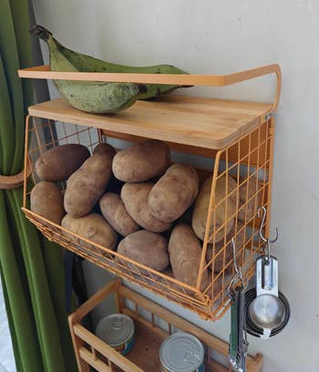 yellow shelf holding potatoes and bananas with hooks on the side holding measuring spoons