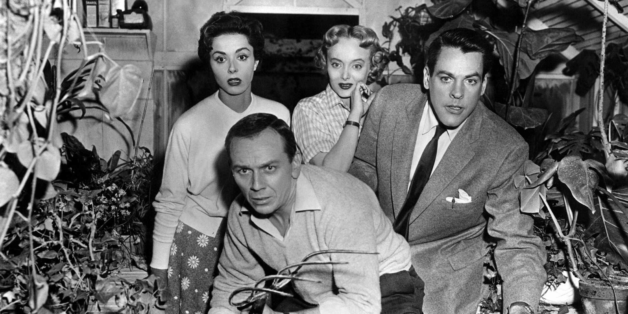 The cast of Invasion of the Body Snatchers look at something in horror while standing in a greenhouse