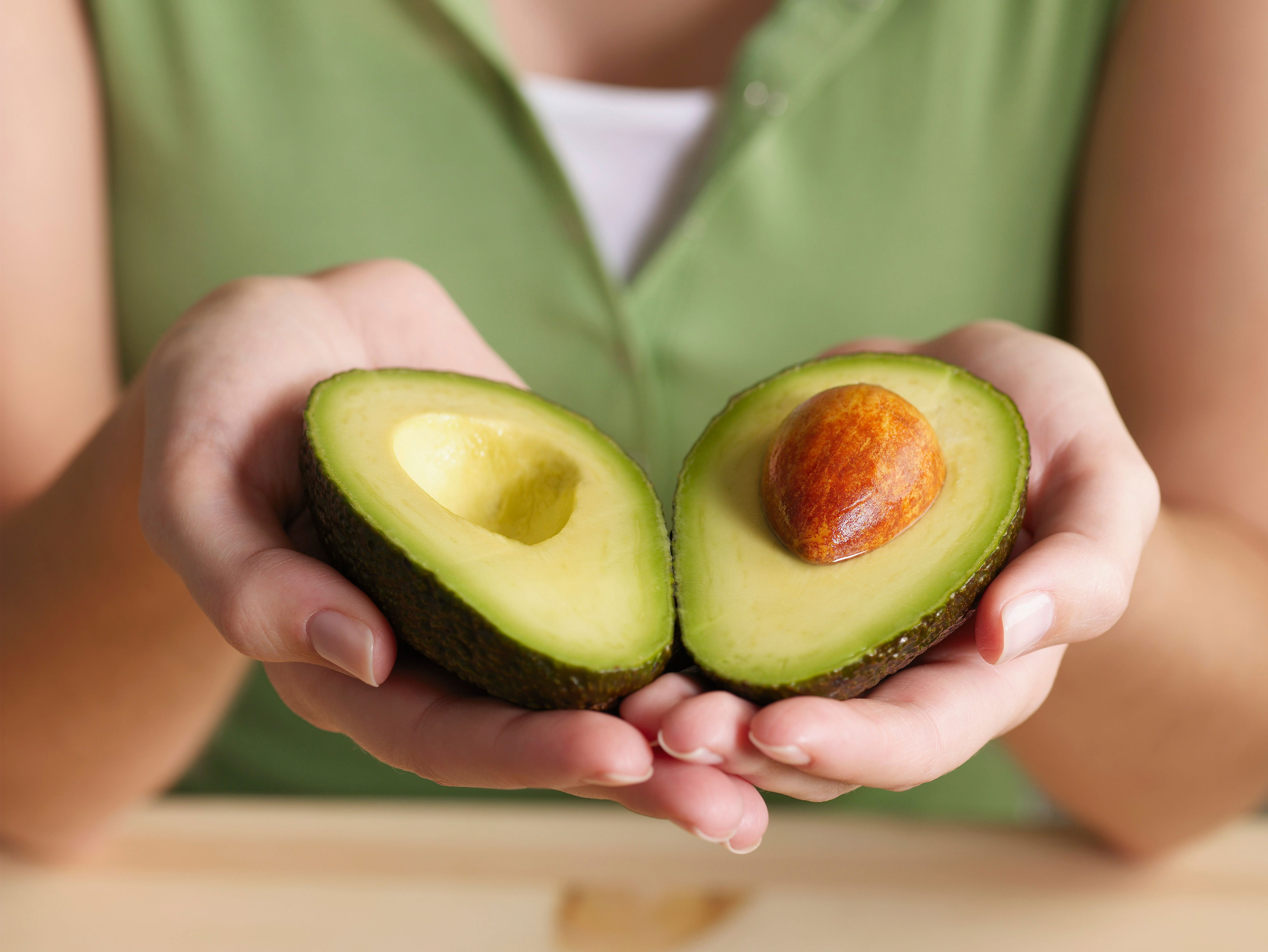 A person holding an avocado that's sliced in half