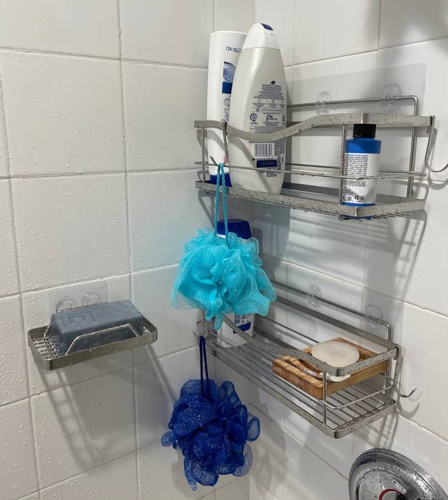 Shower corner with metal racks holding body wash, shampoo, and loofahs, with soap bars are on the third rack