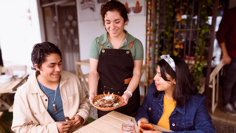 A server bringing a plate of food to diners at a restaurant.