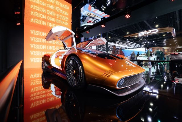A sleek futuristic concept car in vivid orange displayed at an international motor show.