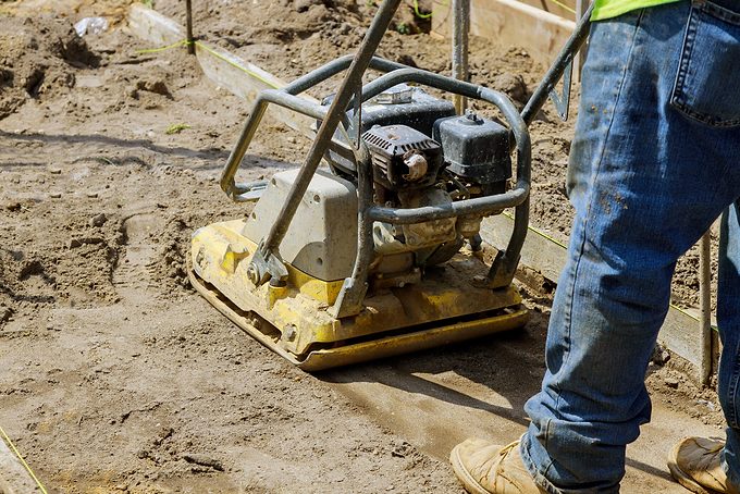 Worker Use Vibratory Plate Compactor Under Construction On New Pavement